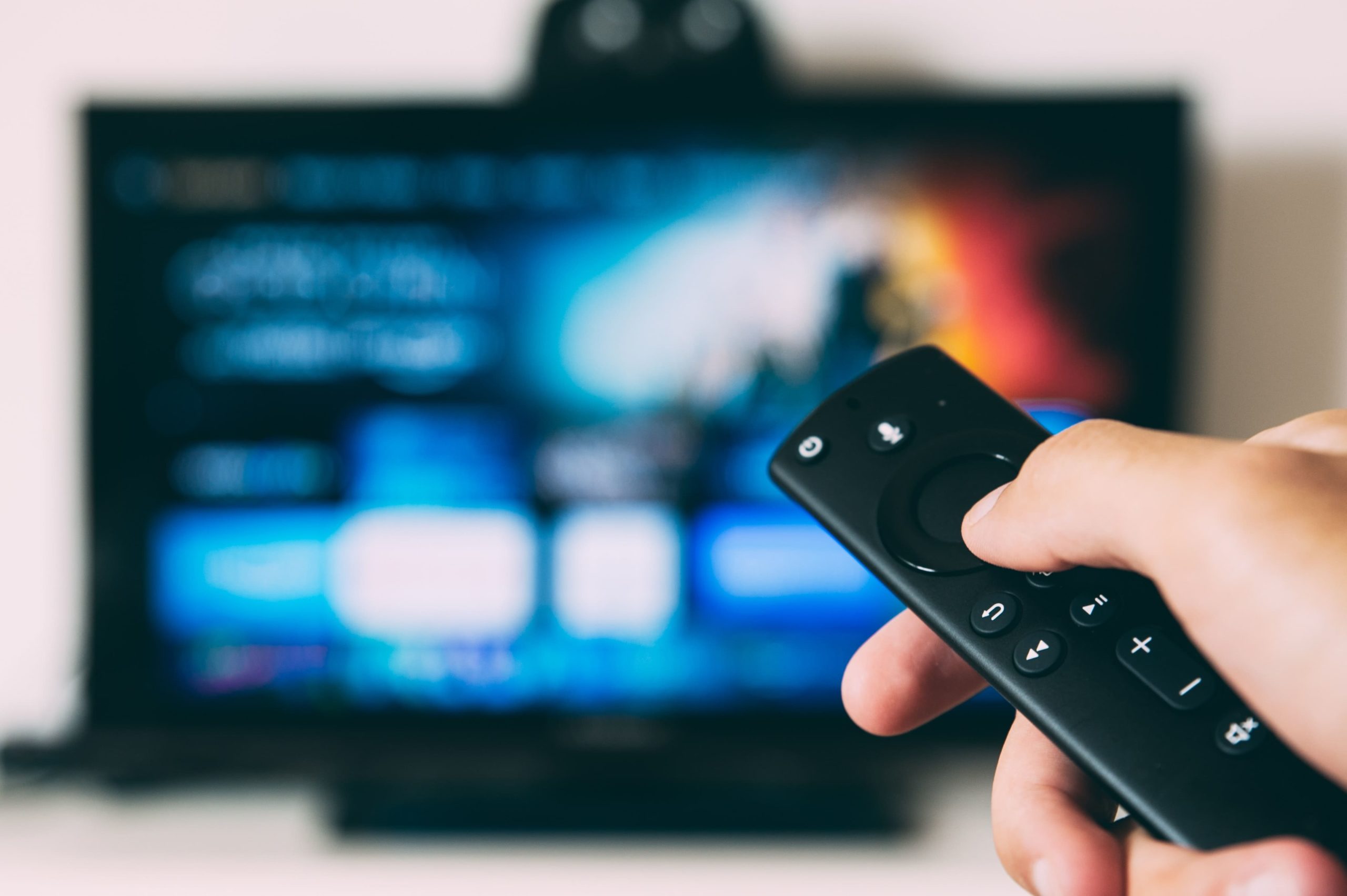 A hand pointing a remote control at a television.
