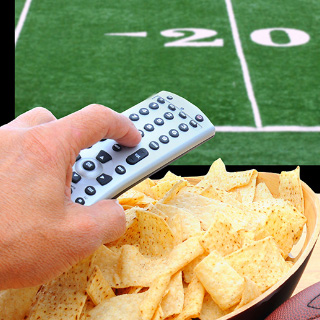 A hand holding a remote control over a bowl of chips