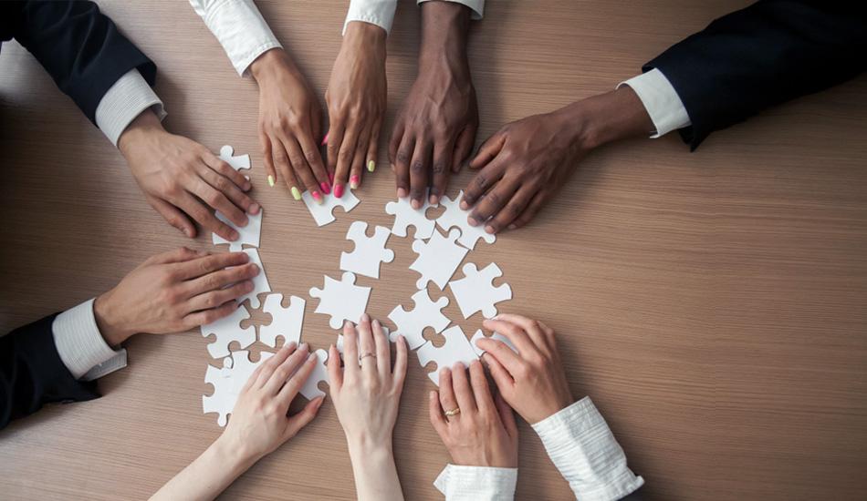 A group of people reaching for puzzle pieces on a table