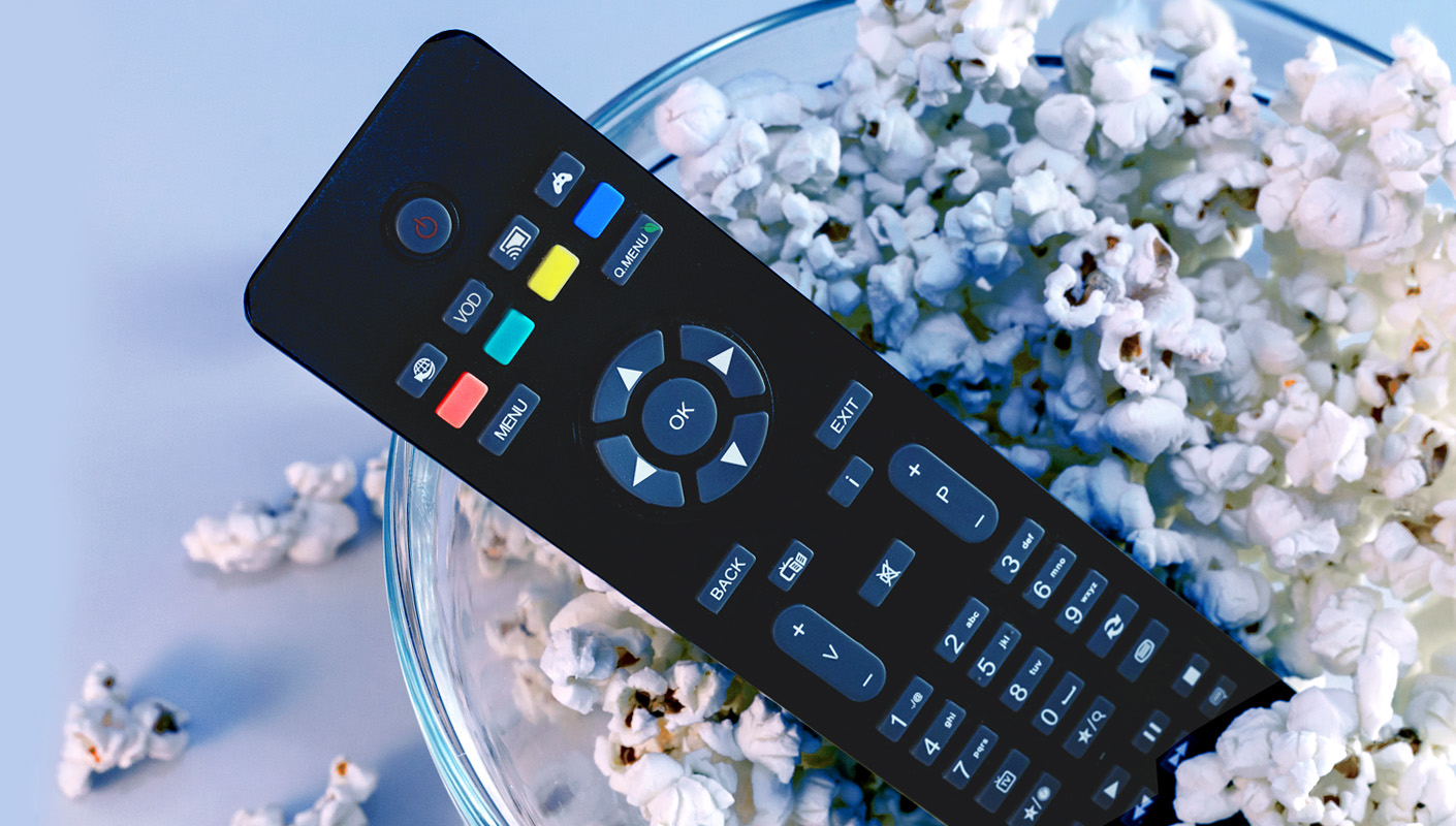 A remote control with multimedia buttons inside a bowl of popcorn.