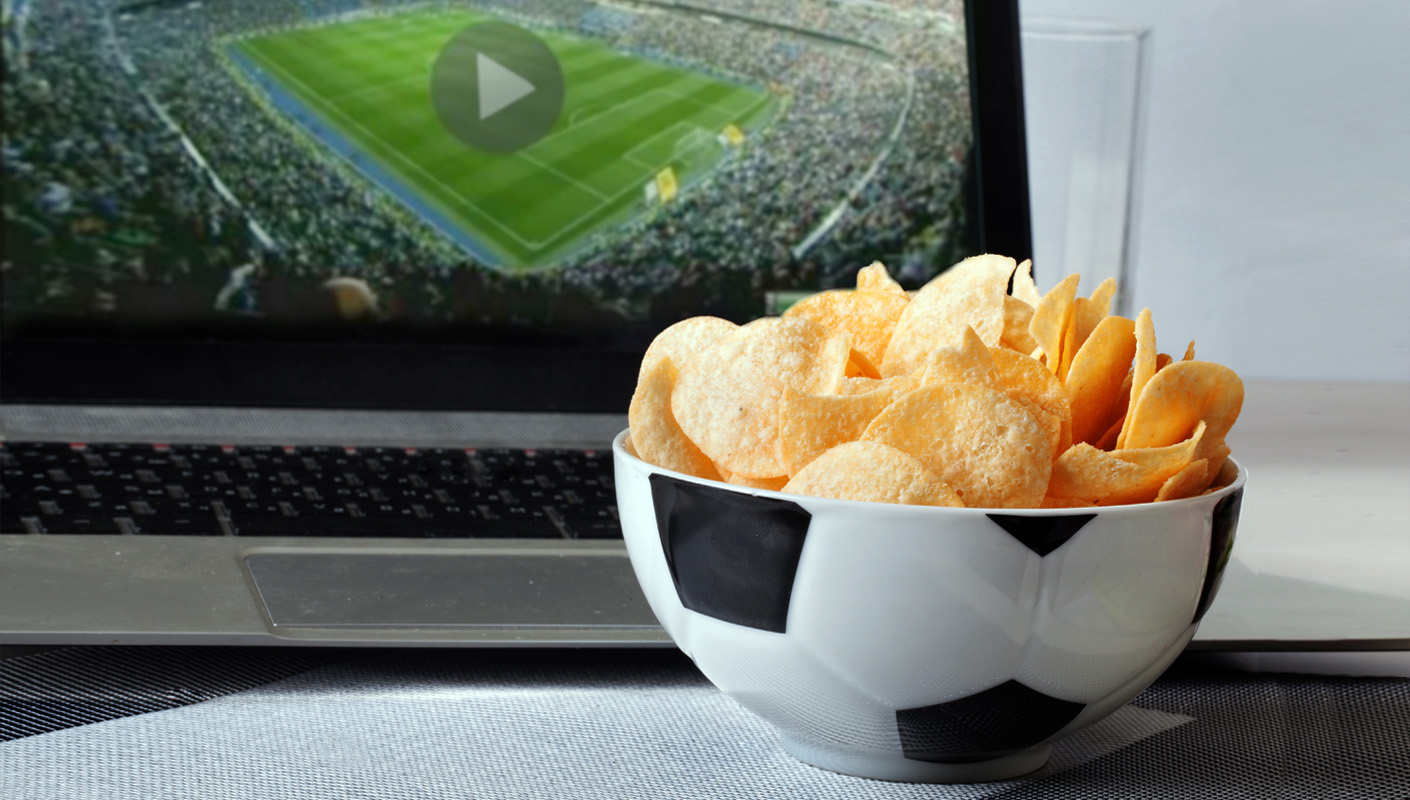 Bowl of chips, the bowl looks like a soccer ball, sitting in front of a laptop that is streaming a live game.
