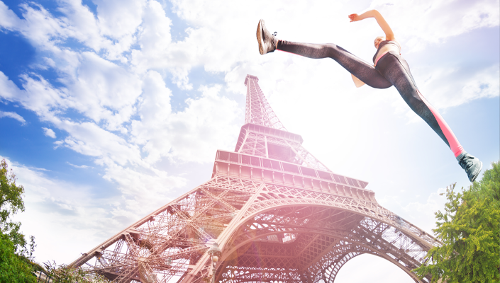 a photo looking up at the Eiffel Tower with what appears to be a woman leaping over it